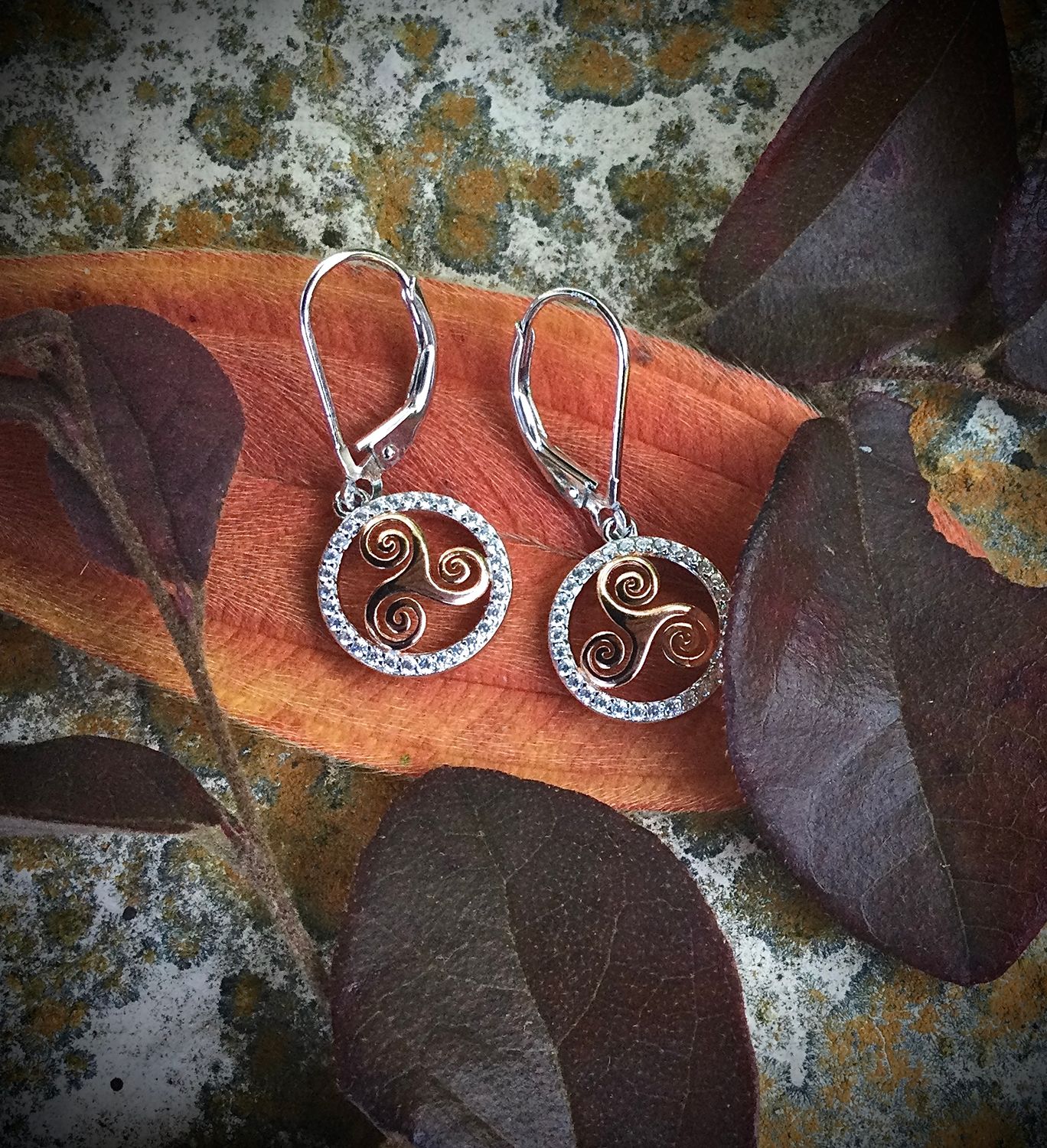 Sterling silver gold-plated Celtic triskele earrings, handcrafted Irish jewelry, on orange leaf.