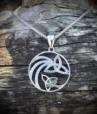 Sterling silver shooting star pendant with sparkling CZ stones and trinity knot, celebrating Celtic heritage, on bark. 