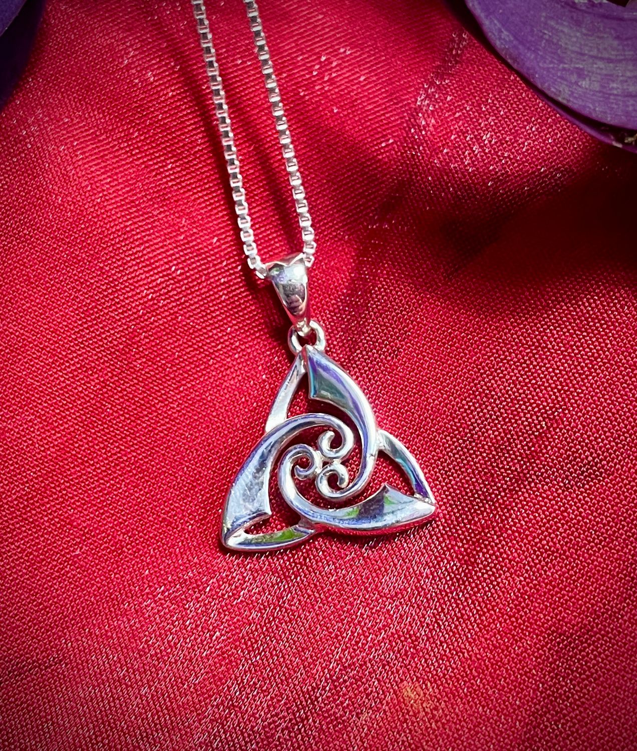 Sterling silver Celtic Trinity Knot pendant with swirl design, handcrafted Celtic jewelry shown on red fabric. 