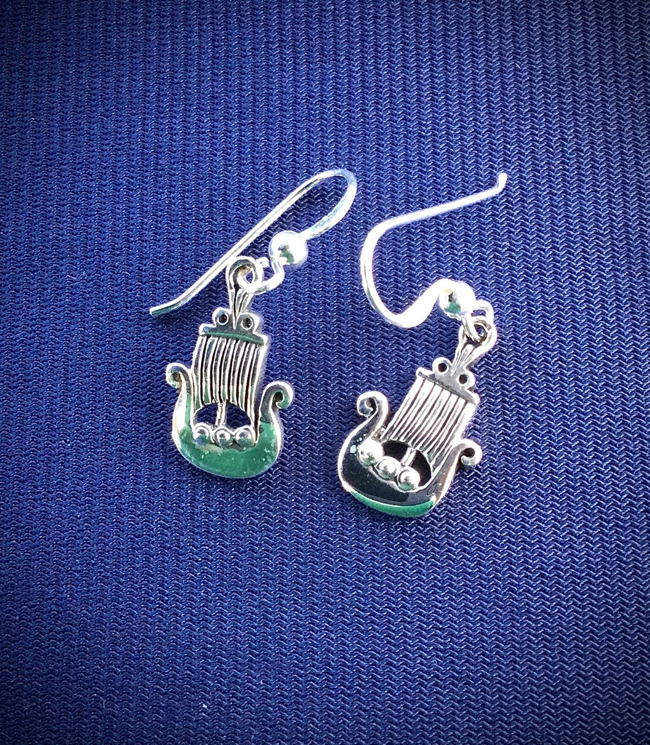 Detailed Celtic Viking Ship drop earrings in polished sterling silver, showcased on blue fabric. 