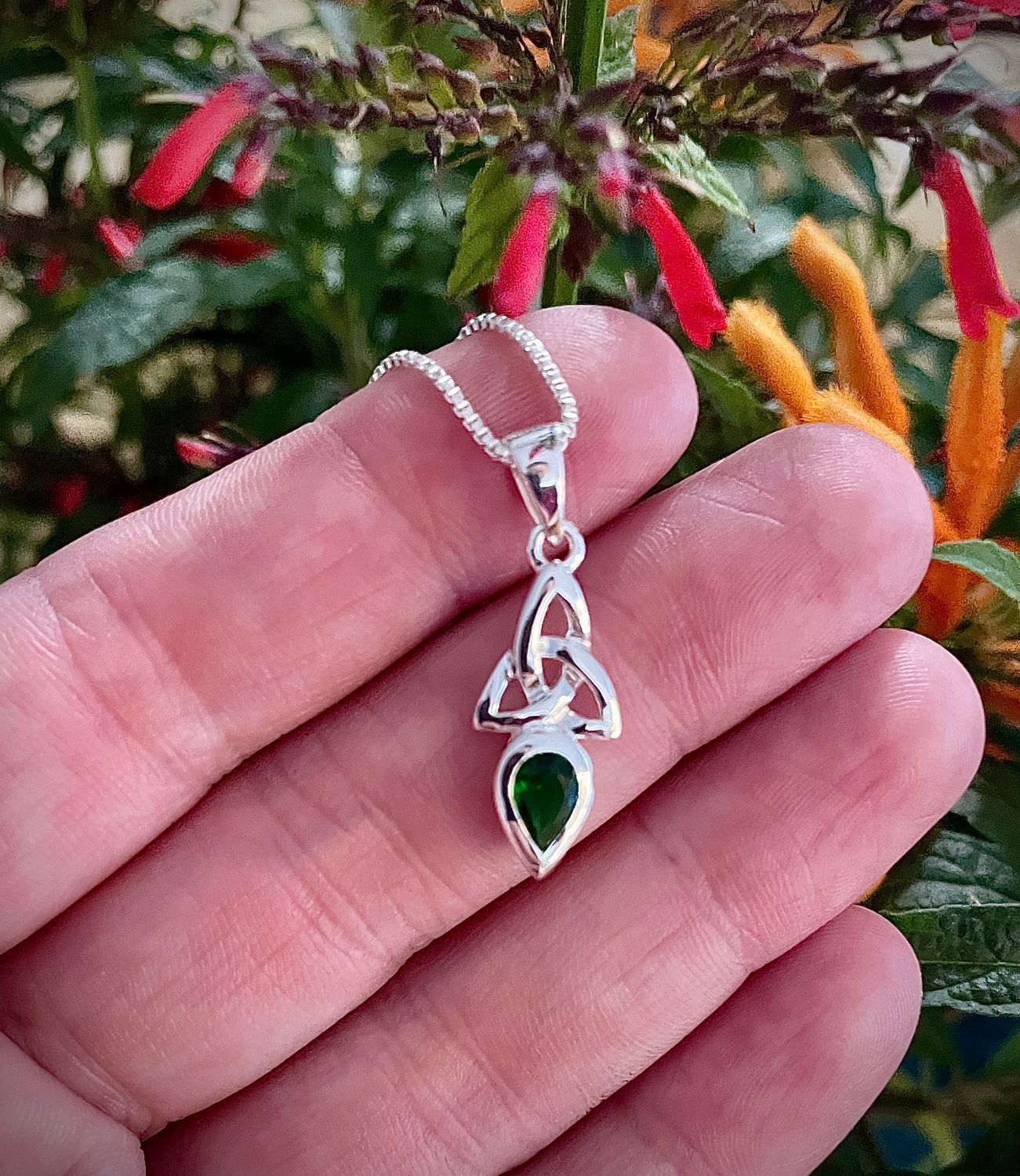Sterling silver trinity knot pendant with a brilliant synthetic emerald stone, on model's hand. 