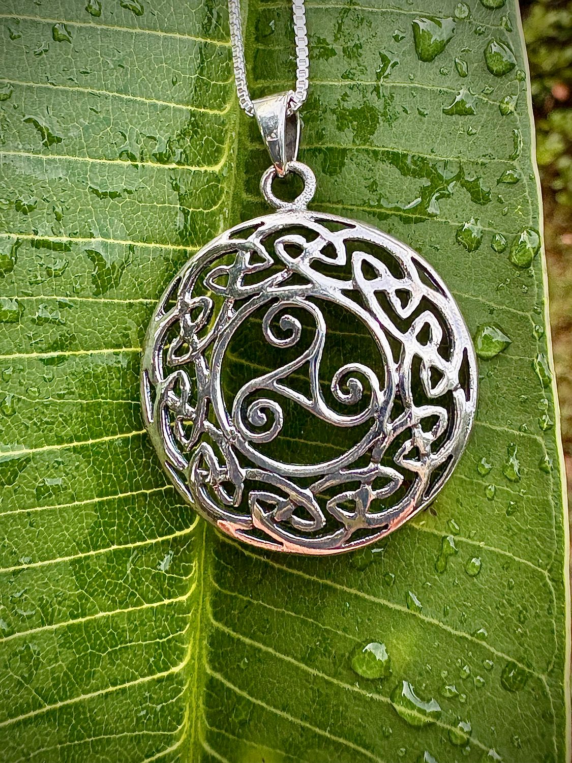 Sterling Silver Celtic Knotwork Pendant with Triskele symbol, representing everlasting motherly love, shown on leaf. 